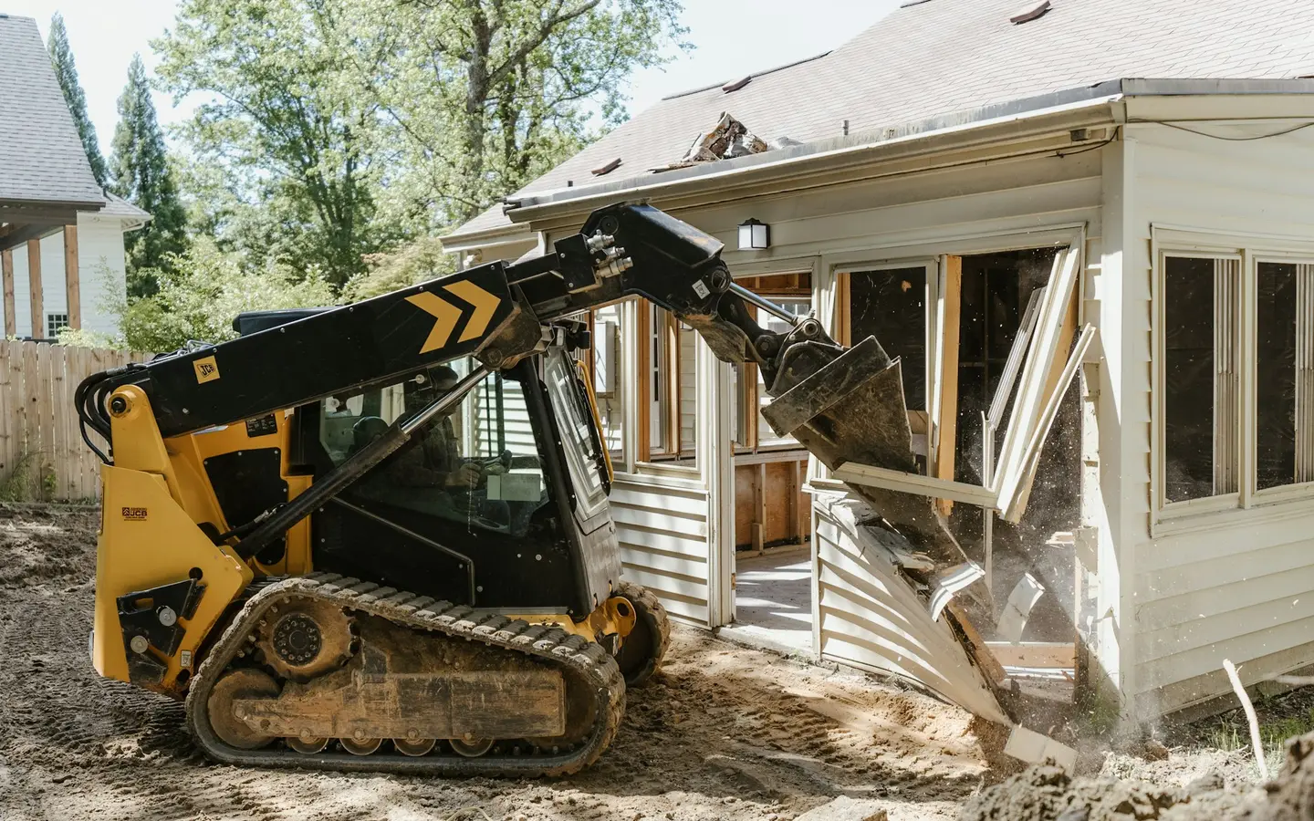 An excavator moving earth directly in front of a residential property