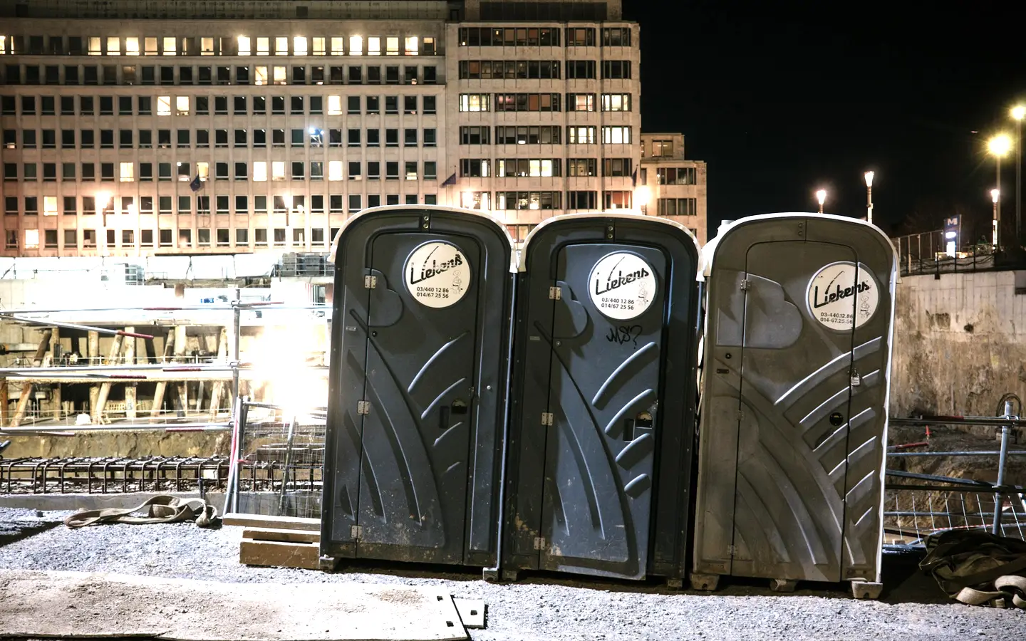 Portable toilets staged at the edge of an active construction site in the evening